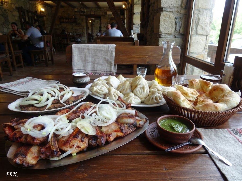 Traditionelle georgische Tischszene im Restaurant mit Mzwadi, Khinkali, Brot, grüner Tkemali‑Sauce und Getränken auf einem Holztisch